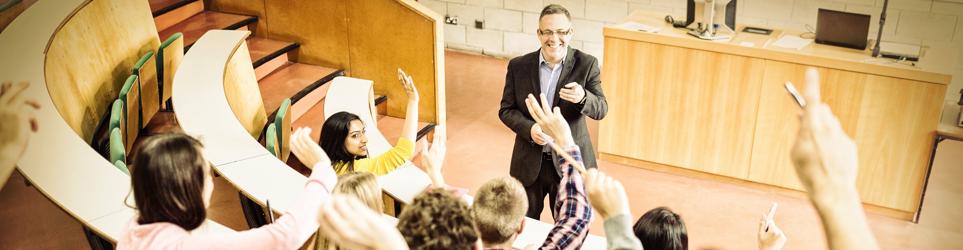 Students raising hands with teacher in lecture hall